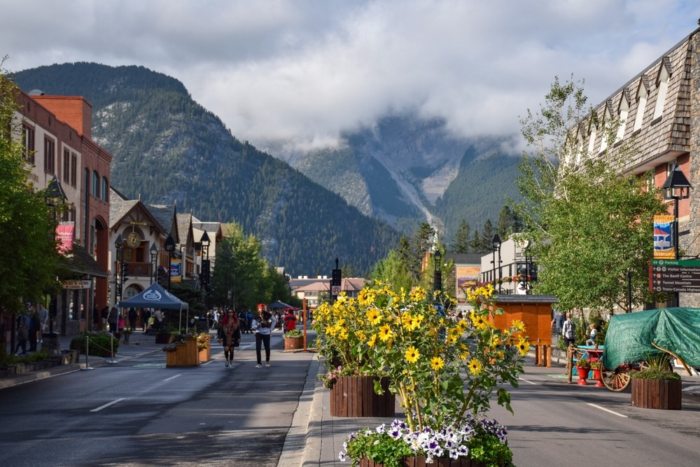 Main Street in Banff during summer with visitors walking through the town and mountains rising in the background