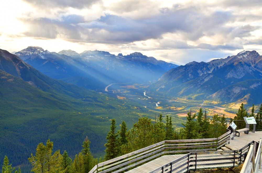 Bow Valley viewed from an upper mountainside viewpoint in the Canadian Rockies, with forest, winding valley contours, and layered mountain ridges.